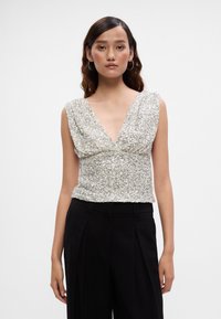 Srebrna bluzica s šljokicama, s V-izrezom i drapiranim materijalom. Uparena s crnim hlačama visokog struka, ističe teksturu i elegantan dizajn.