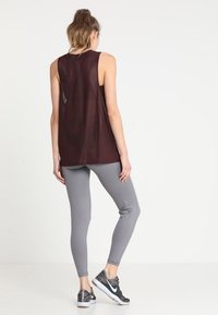 Bordeauxkleurig lichtgewicht tanktop met een open rugontwerp, gecombineerd met strakke grijze leggings. De outfit wordt afgerond met zwart-grijze sportschoenen.