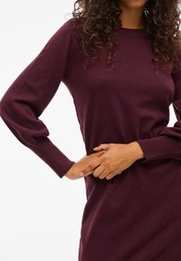 Burgundy-neule, jossa on kevyt rakenne, pitkät puffihihat ja ribbireunat. Kangas näyttää pehmeältä ja joustavalta.