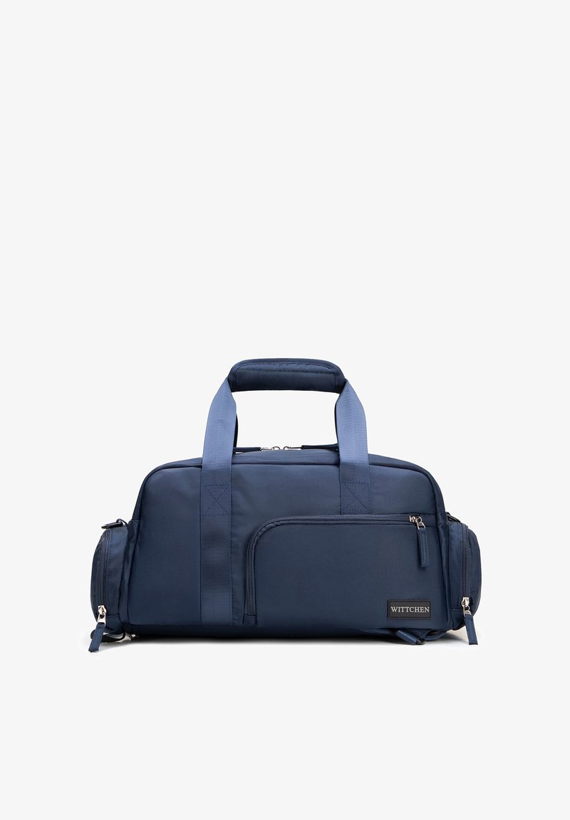 Bolsa de lona rectangular azul oscuro con dos asas, múltiples compartimentos con cremallera incluyendo bolsillos delanteros y laterales, y una pequeña etiqueta de la marca.