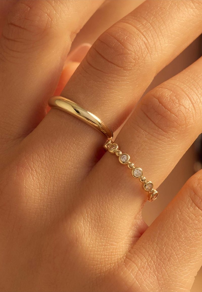 Bague en or et une bague en or ornée de cinq petites pierres circulaires. La main présente une texture de peau lisse et un aspect naturel des ongles.