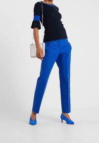 Granatowy top z niebieskim akcentem, rozszerzany rękaw, zestawiony z jasnoniebieskimi, dopasowanymi spodniami i niebieskimi zamszowymi obcasami. Biała torebka z srebrnym łańcuszkiem.