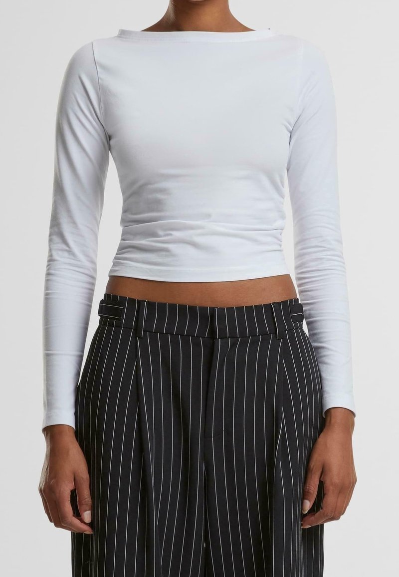 Weißes kurz geschnittenes Oberteil mit langen Ärmeln und weitem Ausschnitt, kombiniert mit schwarzen hochtaillierten Hosen mit Nadelstreifen, die eine glatte Stofftextur zeigen.