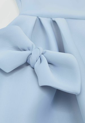 Tissu bleu clair à la texture douce, présentant un grand nœud joliment noué comme détail principal. Des plis sont visibles en arrière-plan.