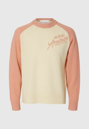 Crèmesweater met roze mouwen en kraag, met "Hotel Amour" geborduurd op de linkerbovenborst in roze letters.