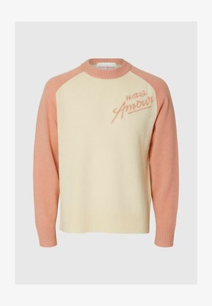 Cremefarbener Pullover mit pinkfarbenen Ärmeln und Kragen, mit der Aufschrift "Hotel Amour" in pinker Schrift auf der oberen linken Brustseite bestickt.