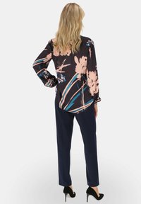 Kwiatowa bluzka z ciemnego materiału w różowe i niebieskie wzory, zestawiona z granatowymi spodniami i czarnymi szpilkami. Długie rękawy z marszczonymi mankietami.