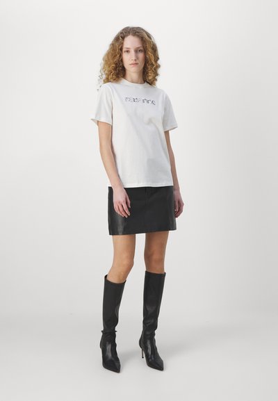T-shirt en coton blanc avec impression de texte sur le devant, associé à une mini-jupe en cuir noir et des bottes noires à hauteur de genou. Texture lisse, design ajusté.