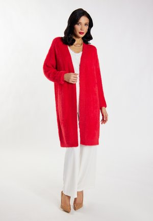 Cardigan rosso fluffoso con maniche lunghe e design aperto, abbinato a una maglietta bianca e pantaloni a gamba larga. Tessuto morbido.
