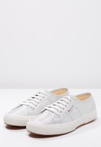 Sneaker argentati con glitter, lacci bianchi, punta arrotondata, parte superiore testurizzata, suola in gomma e dettaglio di branding laterale. Finitura liscia e lucida.