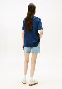 Camiseta de color azul marino con mangas cortas, combinada con pantalones cortos de mezclilla claros. El modelo lleva zapatillas blancas con suela de goma y calcetines blancos.