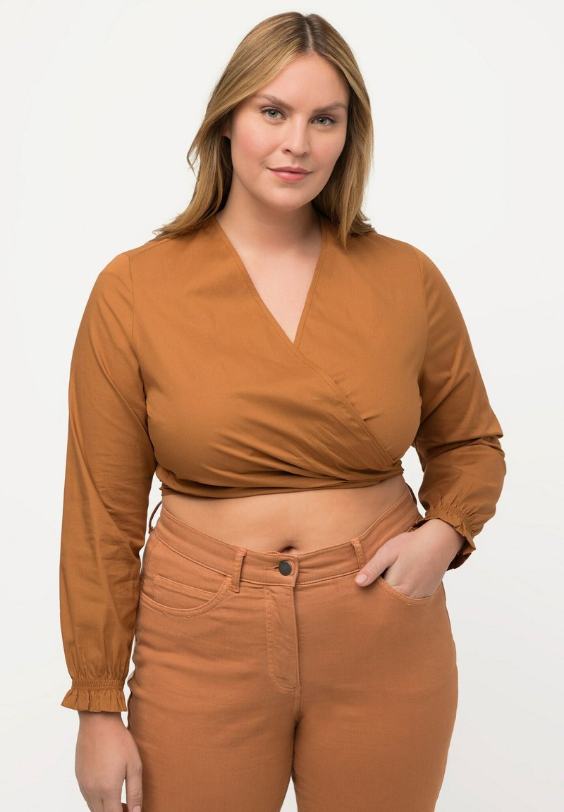 Bruine crop top met lange mouwen en elastische manchetten, gecombineerd met hooggewaiste, slim-fit bruine jeans met zijzakken en een knoopsluiting.