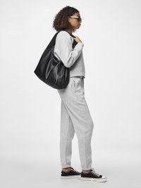 Felpa grigia e pantaloni jogger in morbido tessuto, abbinati a sneakers nere con suola bianca e a una grande borsa a tracolla nera in pelle.