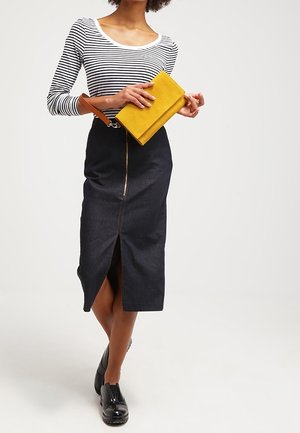 Schwarzer Denim-Bleistiftrock mit einem Schlitz vorne, kombiniert mit einem gestreiften Langarmshirt und einer gelben Clutch mit einem braunen Riemen.