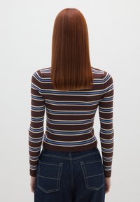 Brauner, langärmeliger Rippstrick-Oberteil mit horizontalen Streifen in Blau und Creme. Getragen mit hochgeschnittenen dunkelblauen Denim-Jeans.