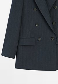 Blazer doppiopetto blu scuro realizzato in tessuto testurizzato con sottili righe verticali. Caratterizzato da bottoni neri e una silhouette su misura.