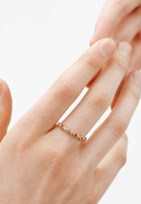 Anillo de oro con piedras preciosas de colores en un patrón a lo largo de la banda, colocado en una mano con piel texturada.
