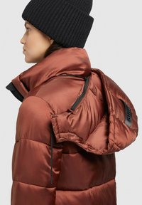 Brown puffer jacket with a shiny finish, featuring a detachable hood, side zippers, and a black ribbed knit beanie.