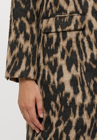 Leopardmønstret kåpe med en teksturert, delt stoff i brunt, beige og svart, med en enkelt lomme foran og lange ermer.