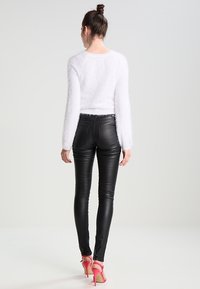 Maglione bianco soffice a maniche lunghe, pantaloni skinny neri lucidi e sandali con tacco rosa. Focus sulla texture morbida e sul design aderente.
