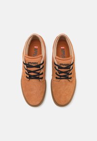 Zapatillas de skate de ante marrón con cordones negros, con una puntera redonda, superficie texturizada y una etiqueta que dice "APPLEYARD" en la lengüeta.