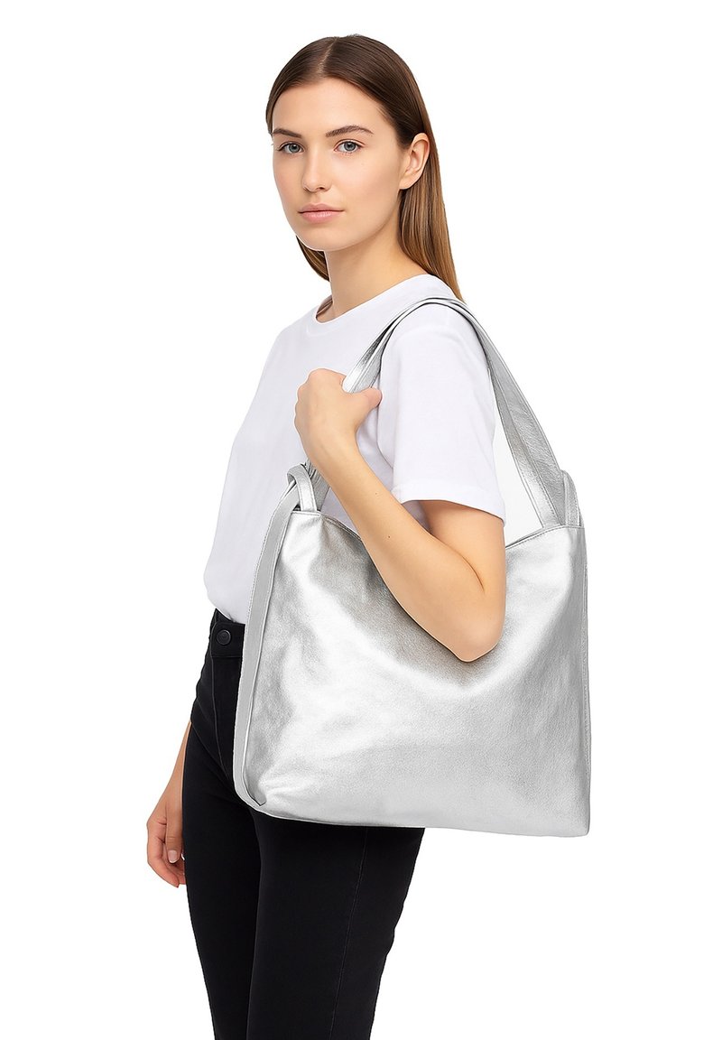 Sac fourre-tout en cuir argenté avec une finition brillante, large bandoulière et forme rectangulaire. Texture lisse avec des détails de design minimalistes.