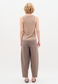 Top senza maniche di un tan scintillante abbinato a pantaloni beige con una vestibilità ampia. Il tessuto ha una leggera lucentezza. Scarpe nere senza lacci completano l'outfit.