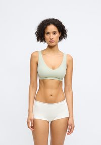 Lys grøn sømløs bh med dyp v-hals design og brede stropper, sammen med hvite boyshorts med blondekant ved midjen.