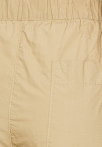 Tessuto beige con una vita elasticizzata cucita e una tasca a toppa rettangolare sul lato destro.