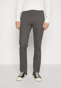 Pantaloni grigi in misto cotone, con vestibilità slim, tasche laterali e chiusura a bottone, abbinati a sneaker bianche e nere.