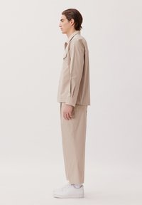 Ensemble composé d'une chemise beige et d'un pantalon en tissu lisse, avec une coupe décontractée, des manches longues et des baskets blanches. Design simple et minimaliste.