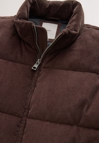 Dark brown corduroy puffer jacket with high collar and silver zipper partially zipped, showing black inner lining and white brand label.