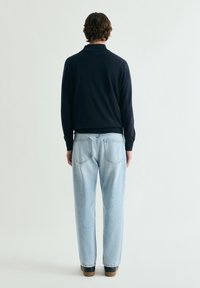 Suéter azul marino con cuello redondo, combinado con vaqueros de corte holgado en azul claro. Zapatos marrones que complementan el look casual. Diseño minimalista, textura suave.