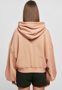 Suure mahuga, pehme virsiku värvi kapuutsiga sviiter, millel on suur kapuuts, ribaga allserv ja langenud õlad, koos tumedate lühikesed pükstega, minimaalne brändi detail.