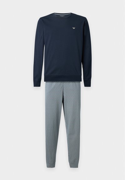 Haut bleu marine à manches longues et col rond avec petit logo sur la poitrine, associé à un pantalon bleu clair à motif géométrique.