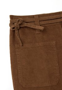 Tela de pana marrón con una superficie texturada, que presenta un cinturón atado y un bolsillo en la cintura, adornado con costuras decorativas.