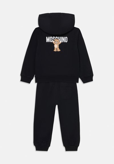 Čierny dvojdielny teplákový komplet s kapucňou, rebrovanými manžetami a grafikou medvedíka s textom "Moschino" na chrbte. Hladká textúra.