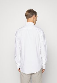 Camicetta bianca a maniche lunghe con colletto a punta, dettagli ai polsini e orlo curvo, realizzata in tessuto di cotone leggero. Design semplice.