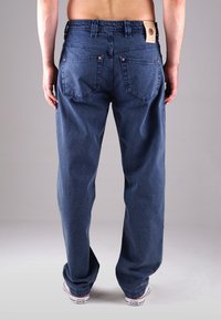 Dunkelblaue Denim-Jeans mit geradem Bein, Gesäßtaschen und einem Lederetikett am Bund. Sie haben kupferne Nieten und sichtbare Nähte.