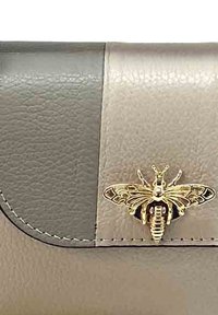 Leren clutch met een gouden bij-embleem, met een gesplitst ontwerp in donkergrijs en lichtbeige. Gladde textuur en gestikte details.