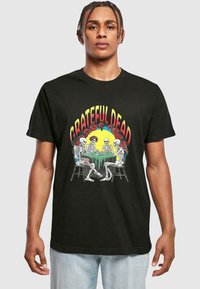 Sort bomulds t-shirt med et farverigt print af skeletter, der spiller kort ved et bord, med teksten "GRATEFUL DEAD" ovenfor og rosen-dekorationer.