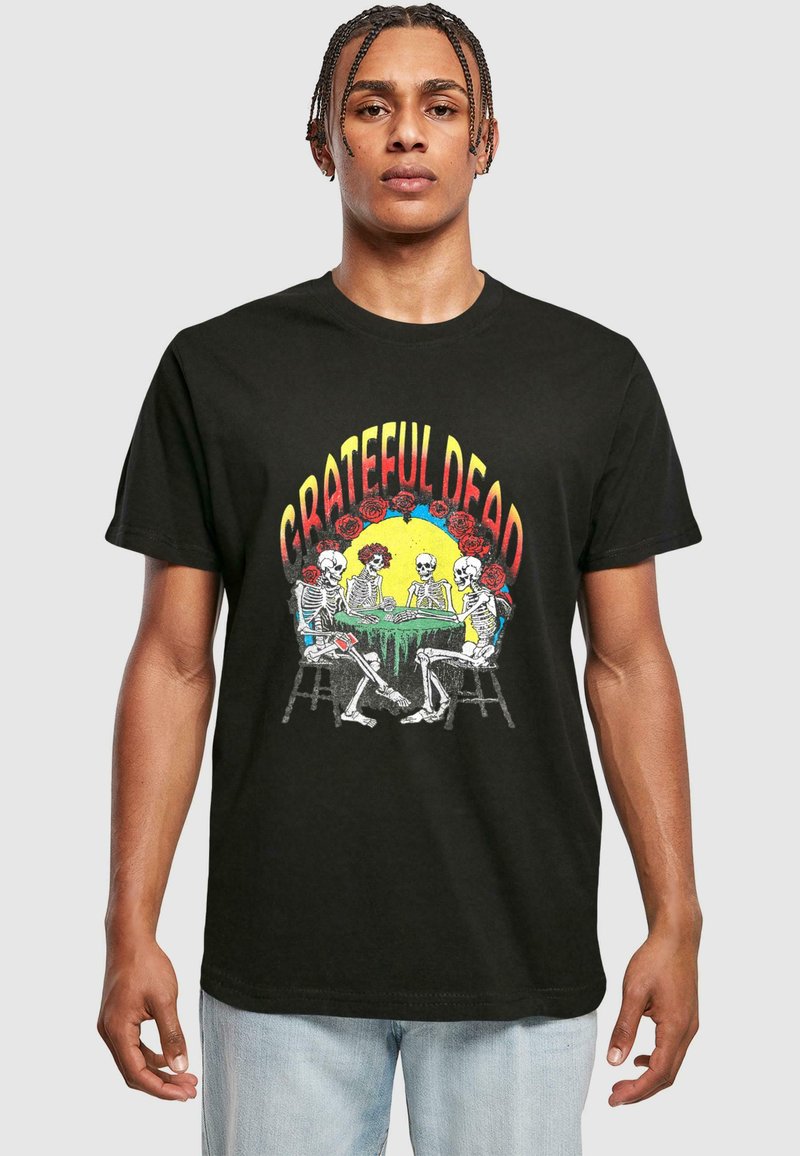 Sort bomulds t-shirt med et farverigt print af skeletter, der spiller kort ved et bord, med teksten "GRATEFUL DEAD" ovenfor og rosen-dekorationer.
