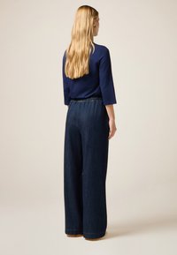 Top navy de mangas tres cuartos combinado con pantalones de denim oscuro de pierna ancha que cuentan con una cinturilla elástica. Textura suave, diseño casual.