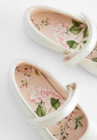 Silberne Glitzer-Ballettschuhe mit einem Riemen, ausgestattet mit einer floral gemusterten Innensohle in rosa- und Grüntönen sowie einer glatten Textur.