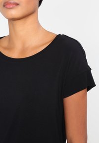 Svart kortärmad topp med vid halsringning och diskret ribbad textur påärmarna. Slät tyg med avslappnad passform.