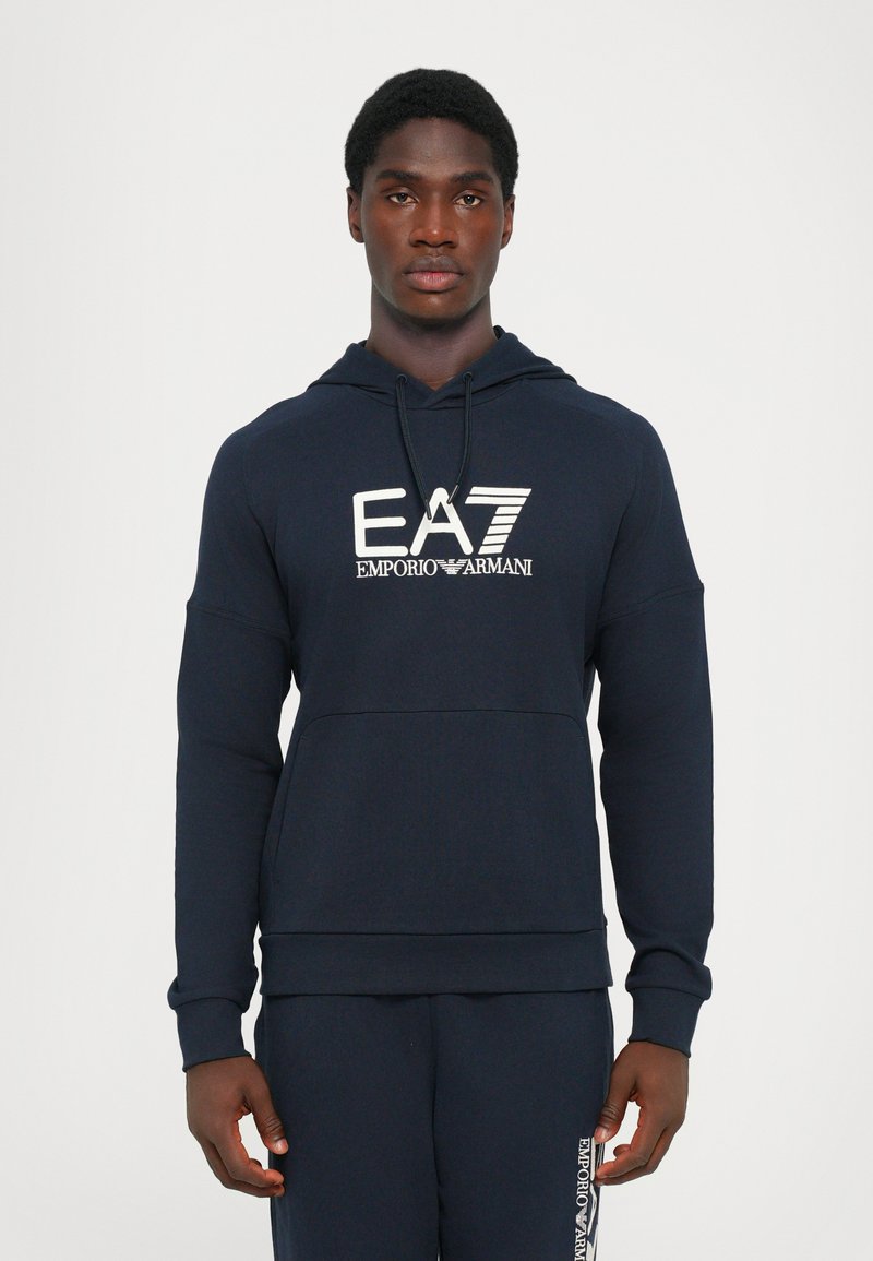 Felpa blu navy con cappuccio e tasca a marsupio, caratterizzata dal logo bianco EA7 Emporio Armani, realizzata in tessuto liscio con polsini a costine.