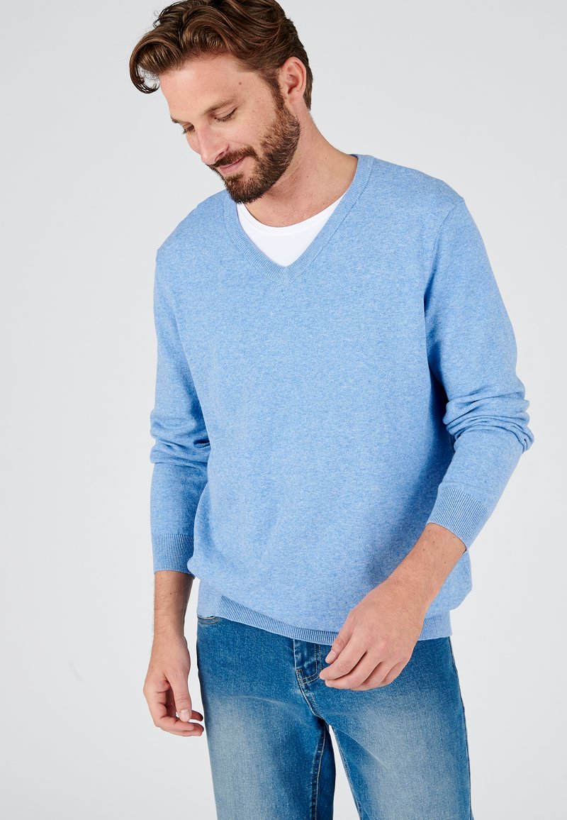 Pull en tricot bleu clair avec un design en V et des poignets côtelés, associé à un jean en denim bleu délavé. Texture douce et coupe décontractée.
