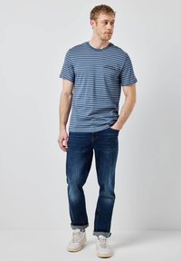 Modrá pruhovaná trička s kulatým výstřihem, kombinované s tmavě modrými džíny a bílými teniskami. Jednoduchý, neformální design s volným střihem.