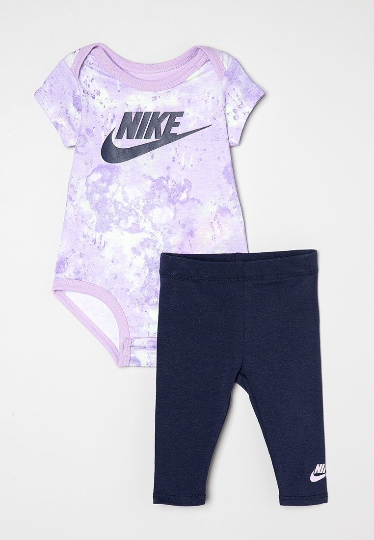Bodysuit pour bébé tie-dye lilas et blanc avec logo noir, associé à un legging bleu marine avec un petit logo Nike blanc près de la cheville.