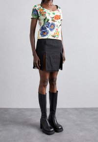 Top de manga corta con estampado floral en color crema, combinado con una minifalda de mezclilla negra con aberturas laterales y dobladillo deshilachado. Botas de plataforma negras hasta la rodilla.